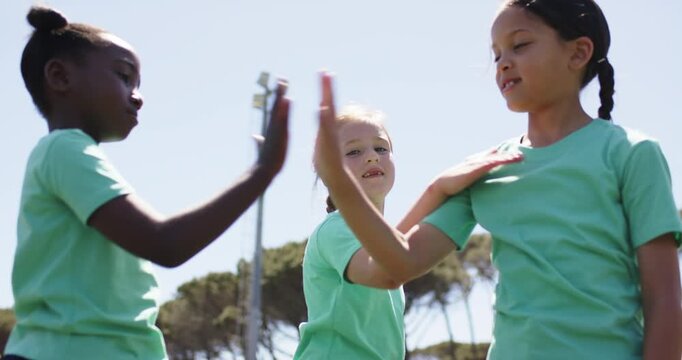 Diverse female child team on grassy field center girl raising hands starting claps in mint shirts