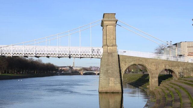 View of the Wilford Suspension Bridge crossing the River Trent in Nottingham, England. This historic pedestrian footbridge links West Bridgford and The Meadows in the East Midlands.