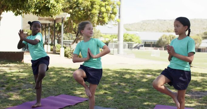 Diverse school-age girls holding tree pose on mats at park right girl starting palm touch balancing