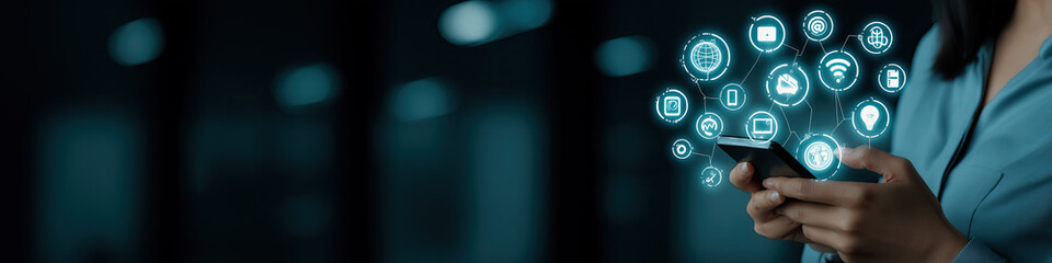 Fototapeta premium A person holds a mobile device displaying holographic icons in a dimly lit workspace.