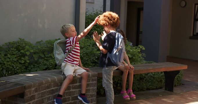 Kids watching standing boy reaching out, two boys with backpacks greeting with high-fives at school