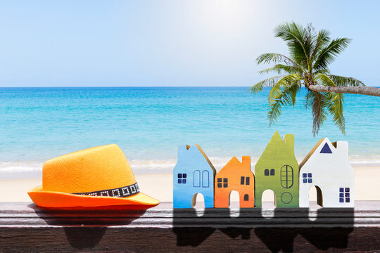 Wooden house model collection with hat on wooden fence over tropical beach background, property and real estate industry