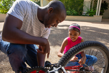 African American father and daughter kneeling on driveway repairing red bike chain and gear © wavebreak3