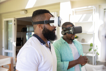 Fototapeta premium African american male friends testing vr headsets standing in living room with sliding glass doors