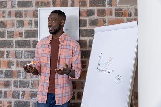 African american man standing beside flip chart explaining graph in office, copy space