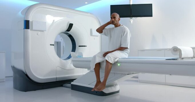 Adult male African descent in gown on scanner table preparing for MRI, adjusting neck, copy space