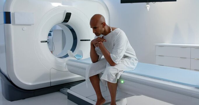 African American man in white gown sitting on scanner table, green light cueing preparing for scan