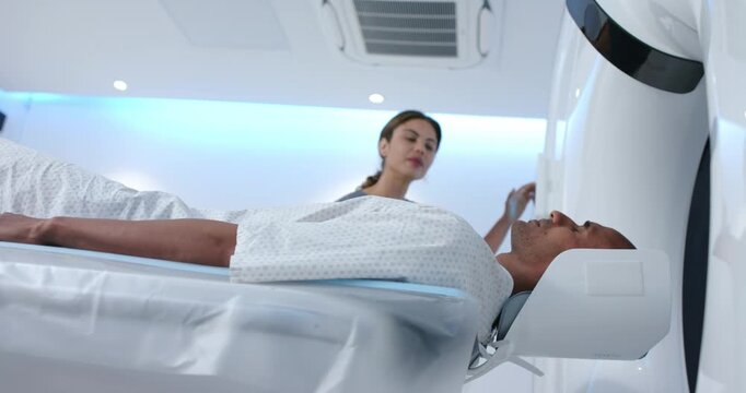 African American tech with male patient, using scanner panel after positioning at gantry for scan