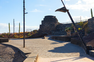 Historic Los Hornos de la Familia Morales, lime kiln site in Puerto del Rosario, Fuerteventura. Ancient stone structure is modern park landscape featuring native plants like cactuses and paved walkway