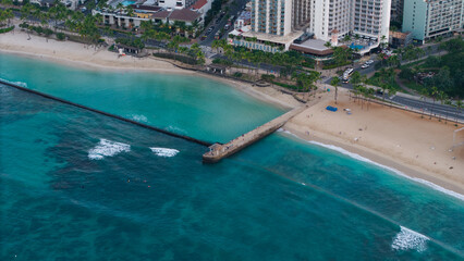 Fototapeta premium Aerial drone view of tropical beach with turquoise ocean water, pier extending into the sea, and coastal city shoreline, scenic island travel destination with clear water and sandy beach