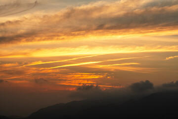 Beautiful bright orange sunset sky with clouds over the mountains silhouette. 