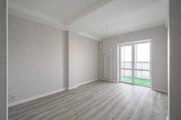 Fototapeta premium bright, empty room with light grey laminate flooring, off-white walls, white ceiling, vertical radiator, large glass door leading to a balcony with green flooring.