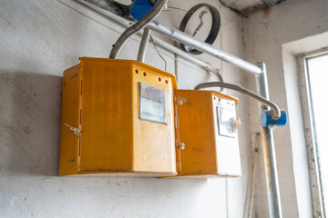 Aging electric meter boxes attached to a damaged wall in an old house, illustrating obsolete power systems, exposed conduits and the general wear typical of older constructions.