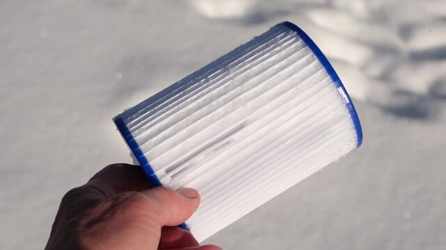 Replacement pool filter cartridge covered with snow in the hand. Clean white snow area. Concept of swimming pool maintenance and water purification. Winter sunlight. Shallow depth of field. 