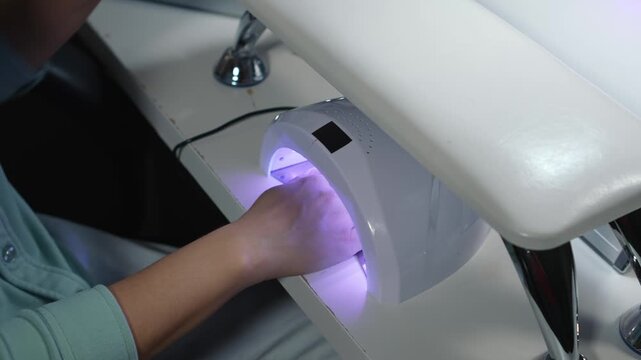 Client cures hand under lamp, ensuring even fixation of nail tips on all fingers using ultraviolet light
