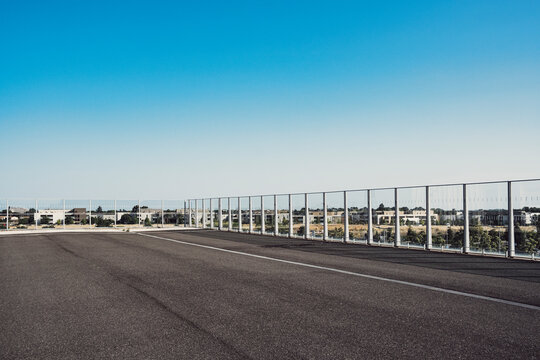 Modern urban architecture empty road of asphalt toward horizon with fence under open sky creating strong perspective and copy space for travel