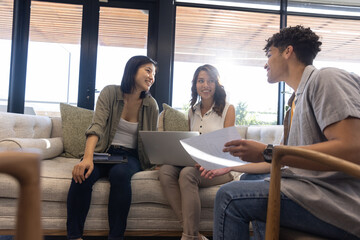 Diverse coworkers discussing with documents, using laptop and tablet on sofa in lounge