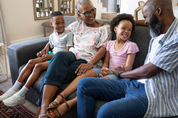 Obraz premium African American family sharing turquoise toy while sitting together on grey sofa in living room