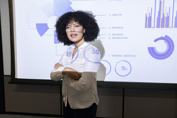 Mid adult woman presenter standing at conference with blouse and charts on screen, copy space