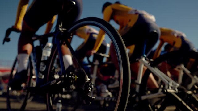 Close-up of racing cyclists with focus on spinning bike wheel. Intense motion and teamwork in competitive outdoor cycling event.