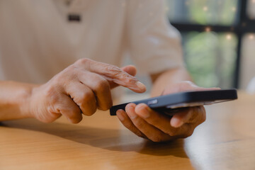 Close-up of hands holding and touching a smartphone on a wooden table. Concept of mobile technology, digital communication, online services, and modern lifestyle.
