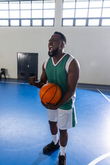 Naklejka premium African american man wearing jersey, shoes holding basketball celebrating on court with lines