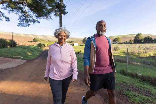 African american senior couple walking on dirt road past wire fence and pasture