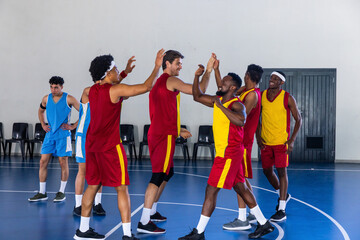 Obraz premium Diverse male basketball players in red-yellow uniforms high-fiving on court near chairs