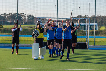 Diverse field hockey teammates with sticks while walking away from goal net on synthetic turf