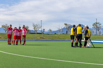 Diverse male field hockey players forming separate huddles on turf pitch with sticks