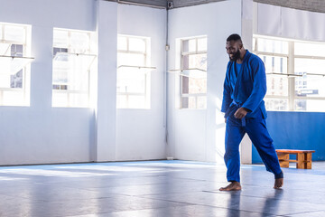 Fototapeta premium African american male martial artist practicing moves across dojo mats in blue gi, copy space