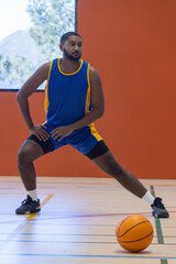 Naklejka premium African american male athlete in basketball uniform stretching on court with basketball