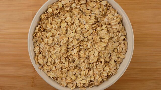 Oat flakes, rolled oats in a white bowl on wooden background top view.