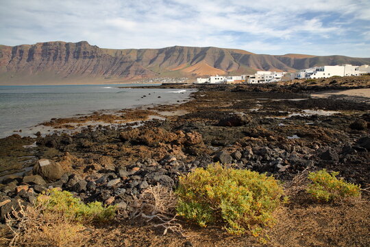 The rocky and volcanic coast and the village Caleta de Famara, Lanzarote, Canary Islands, Spain, with the impressive cliffs of El risco de famara in the background