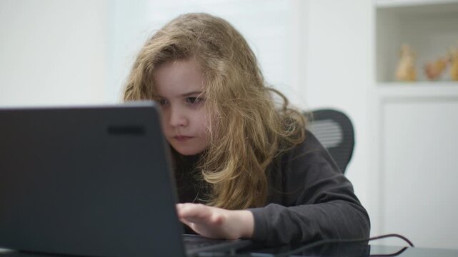 Child learning online on laptop. Child focused on laptop education. Child practicing skills on laptop. Child studying digitally on laptop. School kid study online.