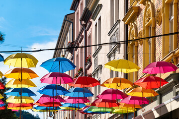 Floating colorful umbrellas above alley in Děč&iacute;n, Czech Republic, with decorated facades and summery lighting