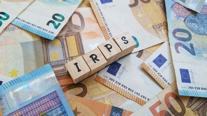 IRPS acronym made of wooden letter cubes on pile of Euro banknotes.  Imposto sobre os Rendimentos das Pessoas Singulares (Personal Income Tax)