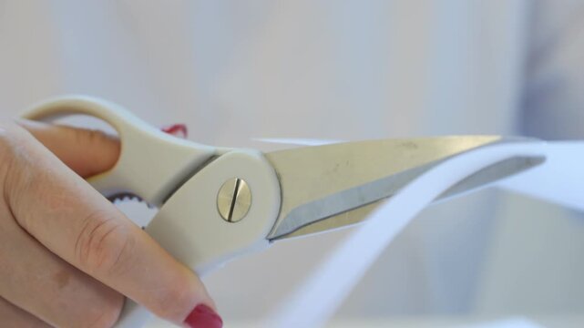 Pair of scissors is being used to cut a piece of paper. The scissors are silver and white