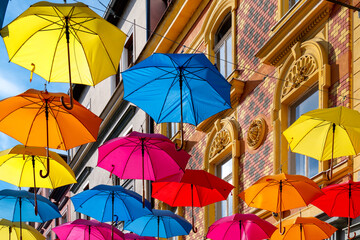 Floating colorful umbrellas above alley in Děč&iacute;n, Czech Republic, with decorated facades and summery lighting