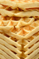 A close up shot showing a high stack of freshly baked golden brown waffles with detailed square...
