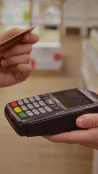 Vertical close up shot of unrecognizable female customer completing contactless payment by card while retail staff holding POS terminal at beauty shop