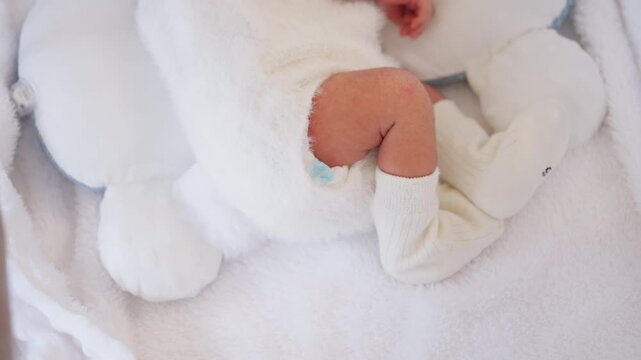 Close-up of newborn baby legs in white socks and fleece outfit on a soft white blanket. Warm, clean, and gentle moment representing infant care and tenderness.