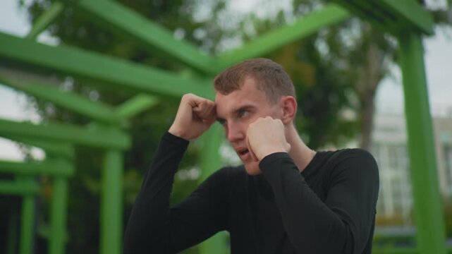 white man under green structure boxing, concentrated shadowboxing drills with raised fists and quick jabs, urban outdoor gym vibe with metal beams, closeup profile captures technique and breath,
