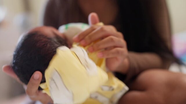 A woman is holding a baby in her arms. The baby is wearing a white shirt. The woman is holding the baby's head