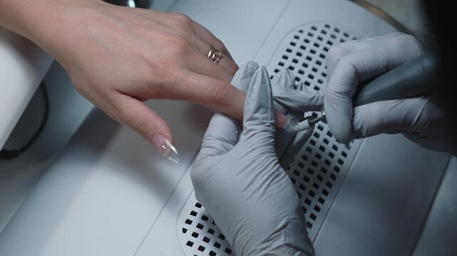 Shaping clear nail extension tip using electric nail file tool for precise length and perfect result in nail salon
