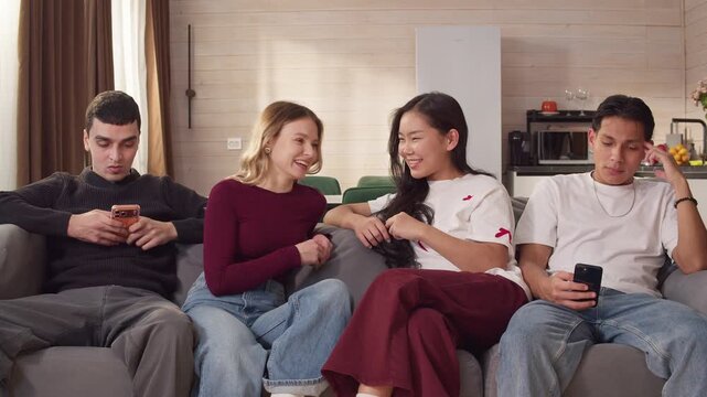 Multiethnic group of young adult friends sitting sofa, two men using mobile cellphone while women talking. Concept modern communication. Phone addiction. Awkward acquaintance moment. Couple meeting.