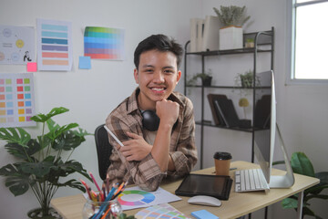 Smiling Young Male Graphic Designer Sitting at His Modern Desk With Stylus and Headphones