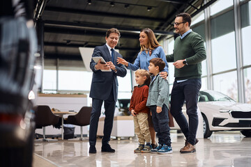 Obraz premium Happy salesman using touchpad with a family at car dealership.