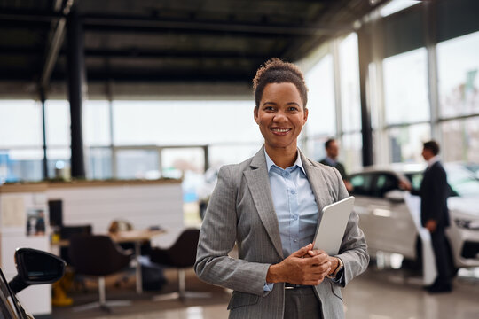 Happy black saleswoman at car dealership looking at camera.