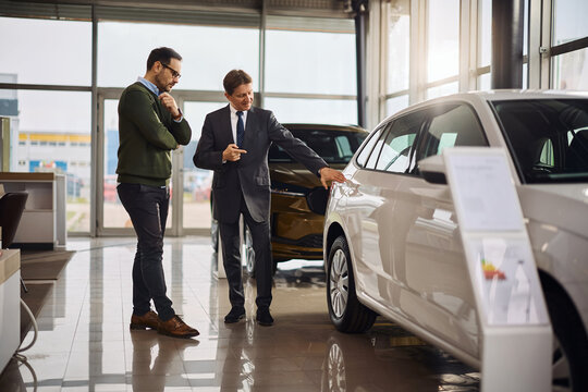 Smiling salesman explaining the features of a new car to his customer in showroom.
